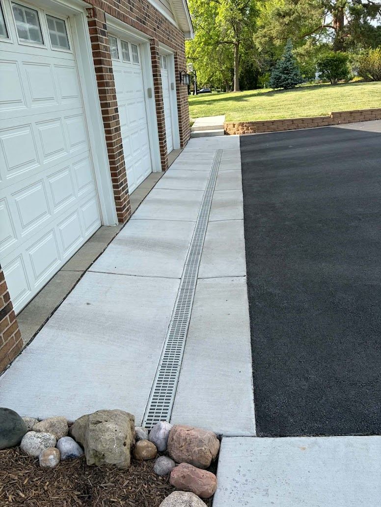 Linear trench drain set between concrete pad and asphalt driveway by G&D Construction